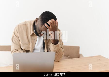 Il giovane uomo nero ha lavorato in modo eccessivo, soffrendo di mal di testa mentre si siede al portatile a casa Foto Stock