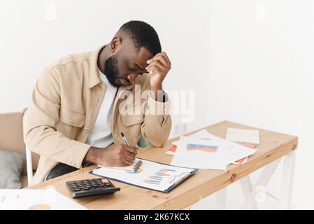 Afro americano giovane uomo molto frustrato con i problemi di bilancio della famiglia mentre controlla i documenti bancari o le forme fiscali Foto Stock