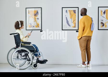 Giovane donna in sedia a rotelle che ascolta la guida con un uomo vicino mentre visitano la galleria d'arte Foto Stock