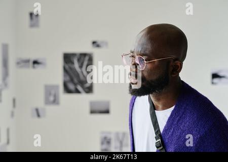 Primo piano del giovane africano in occhiali che esaminano l'arte moderna sul muro della galleria Foto Stock