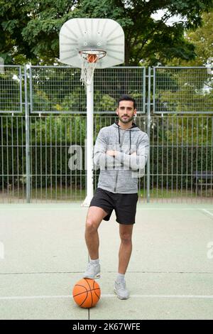 Ritratto di un giocatore di basket amatoriale con il piede su una palla in un campo di basket all'aperto Foto Stock