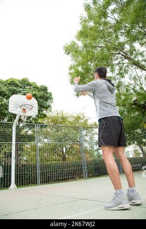 Foto verticale di un giocatore di basket che si allena da solo in un campo pubblico all'aperto Foto Stock