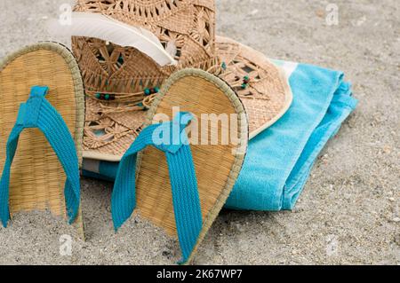 Asciugamano blu, sandali e cappellino di paglia nella sabbia orizzontale Foto Stock