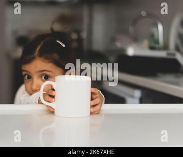 Mug Mockup. contenitore bianco per sublimazione. bambina che tiene la tazza in cucina. Immagine disponibile per i venditori di tazze e i designer. Foto Stock