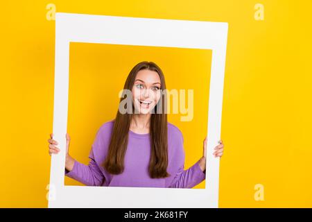 Foto di bella donna overjoyed buon umore due braccia tenere bianco cornice foto studio salone spazio vuoto isolato su sfondo giallo colore Foto Stock