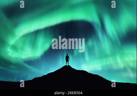 Aurora boreale e silhouette di uomo in piedi sulla montagna Foto Stock