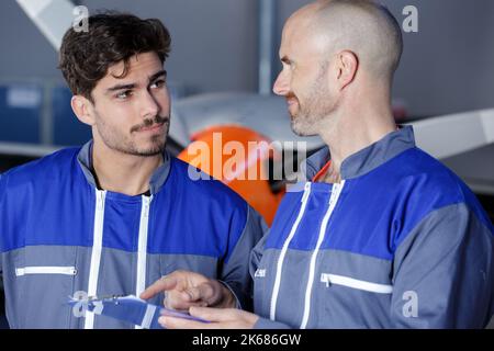 due colleghi di sesso maschile che indossano tute che guardano gli appunti Foto Stock