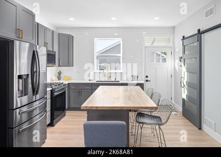 Una cucina con armadi grigio scuro, grande isola con un piano in legno, e elettrodomestici in acciaio inossidabile. Foto Stock