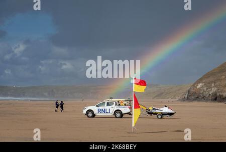 Un arcobaleno che splende su un veicolo RNLI a Perranporth, Cornovaglia. Jet ski e bandiere di avvertimento anche Foto Stock