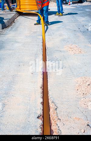 Il lavoratore inserisce cavi in fibra ottica interrati in una micro trincea Foto Stock