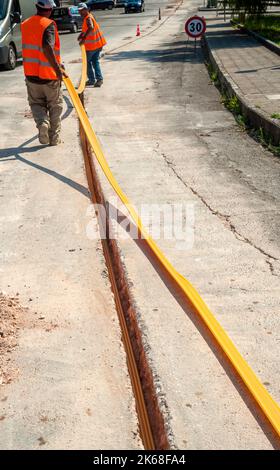 Il lavoratore inserisce cavi in fibra ottica interrati in una micro trincea Foto Stock