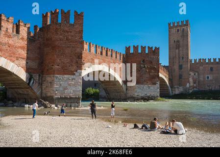 Ponte di Verona, vista panoramica in estate di persone che si rilassano lungo il fiume Adige vicino al medievale Ponte Scaligero nella storica città di Verona Foto Stock