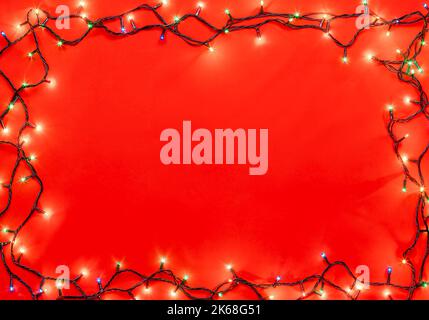 Semplice cornice di Natale fatta di luci di Natale di diversi colori su sfondo rosso Foto Stock