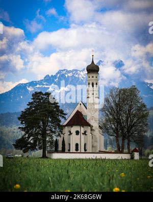 Una foto verticale della chiesa di San Colomano con il monte Tegelberg sullo sfondo a Schwangau, Baviera, Germania Foto Stock