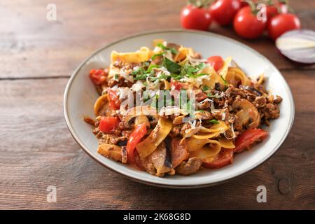Tagliatelle con salsa di carne tritata, pomodori e verdure in stile bolognese, con parmigiano e prezzemolo su un piatto e un tavolo rustico in legno, c Foto Stock