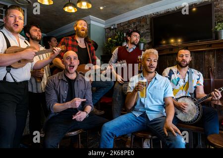 Coro del gruppo Man cantando, suonando musica e bevendo birra in un pub, Grassmarket, Edimburgo, Scozia, Regno Unito Foto Stock