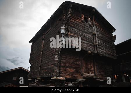 Antico granaio di raccard svizzero tradizionale in legno su pali di pietra nel vecchio quartiere di Hinterdorf di Zermatt Svizzera, tempo piovoso. Foto Stock