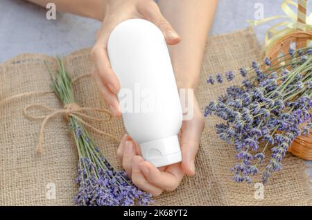 Provetta bianca vuota con crema idratante alla lavanda nelle mani femminili. Crema idratante alla lavanda. Vuoto per la pubblicità Foto Stock