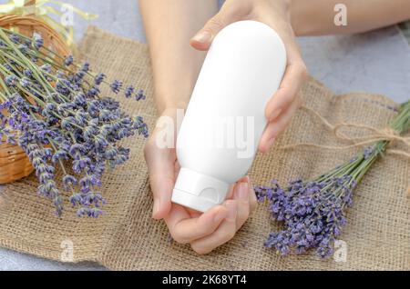 Provetta bianca vuota con crema idratante alla lavanda nelle mani femminili. Crema idratante alla lavanda. Vuoto per la pubblicità Foto Stock