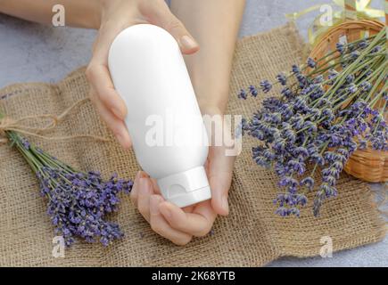 Crema idratante alla lavanda. Provetta bianca vuota con crema idratante alla lavanda nelle mani femminili. Vuoto per la pubblicità Foto Stock