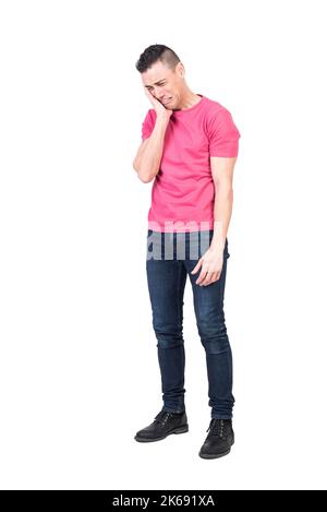 Triste giovane uomo che tocca il viso e piange in studio Foto Stock