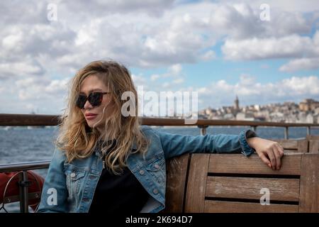 Giovane bella ragazza bionda turistica che viaggia sul ponte del traghetto con la vista sul Bosforo sullo sfondo. Foto Stock