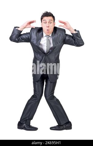 Tutta la lunghezza del giovane impiegato divertente maschio con i capelli scuri che fanno la faccia e gesturing contro lo sfondo bianco Foto Stock