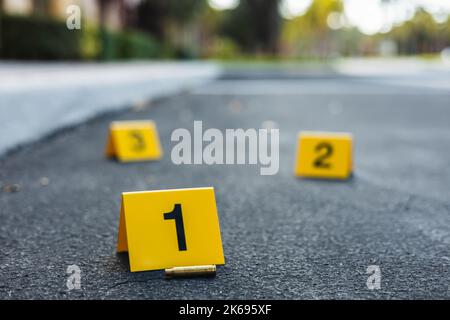 Un gruppo di indicatori gialli della scena del crimine sulla strada dopo una pistola che sparava al fucile d'involucro di proiettile d'ottone Foto Stock