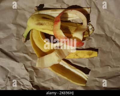 Banane e bucce di mela, rifiuti biodegradabili su carta da imballaggio stropicciata Foto Stock