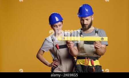 I lavoratori edili che utilizzano strumenti di livello dell'acqua per misurare la superficie piana, lavorando alla ricostruzione per essere uniformi ed equilibrati. Strumento di livellamento da banco per misurazioni stabili. Foto Stock