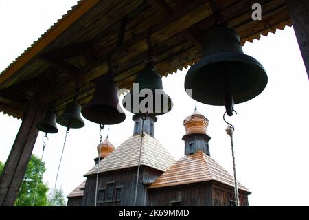 Campane vicino alla chiesa. Massicce campane di preghiera in ghisa sullo sfondo di una chiesa cristiana ortodossa in legno. Antica chiesa cattolica Foto Stock