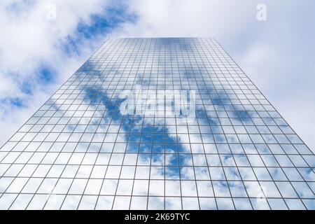 Le nuvole e il cielo blu si riflettono su un alto grattacielo in vetro a specchio Foto Stock