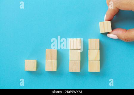 Blocchi di legno con una mano umana mettendo un cubo in cima su sfondo blu. Foto Stock