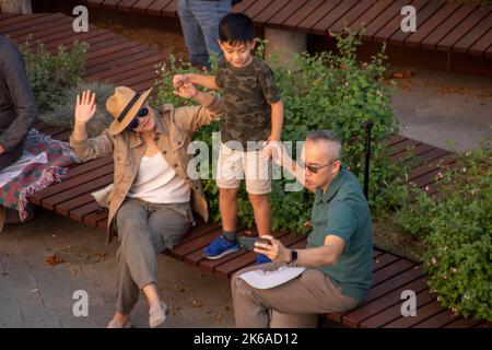 Godendo la musica ad un concerto all'aperto con i suoi genitori a Costa Mesa, CA, un ragazzo asiatico americano danza su una panchina. Foto Stock