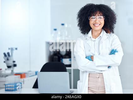 Ritratto di orgoglioso scienziato afroamericano che indossa occhiali di protezione nel suo ufficio. Sorridente medico professionista con le braccia incrociate indossando un laboratorio Foto Stock