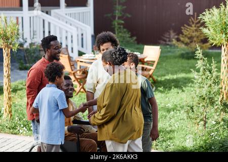 Ritratto di una grande famiglia afroamericana con una persona in sedia a rotelle che chiacchiera all'aperto durante la festa estiva Foto Stock