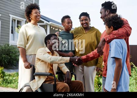 Ritratto con vista laterale di una grande famiglia afroamericana con una persona in sedia a rotelle che accoglie gli ospiti per la festa estiva Foto Stock