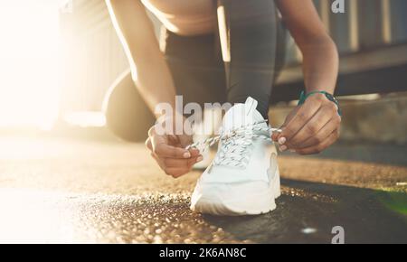 Primo piano di una donna di razza mista legando le scarpe mentre si esercita all'aperto. Scarpe da sneaker bianche con chiusura atleta per una vestibilità comoda e comoda Foto Stock