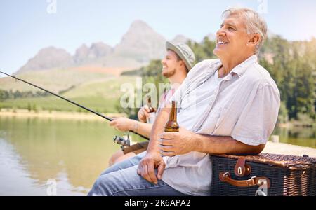 Questo è ciò che si chiama un buon momento: Un uomo anziano che beve birra con suo figlio mentre pesca insieme in un lago in una foresta. Foto Stock