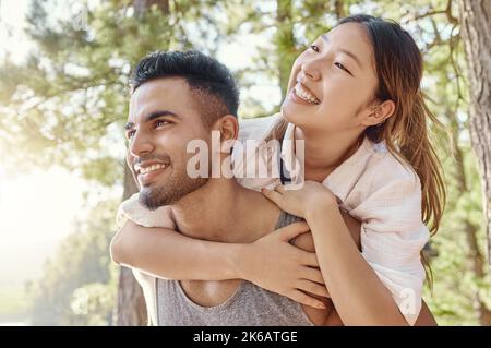 Questo è il motivo dei fidanzati: Un bel giovane che dà alla sua ragazza un giro in piggyback durante una giornata nei boschi. Foto Stock