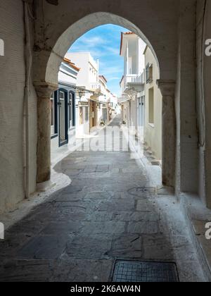 Grecia, Andros isola, Cicladi. Vista dalla stonewall coperta ad arco dei vicoli lastricati in pietra blu del cielo e delle case imbiancate nella città di Chora. Verticale Foto Stock