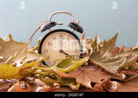 Ritorno all'ora legale. Sveglia nera e foglie autunnali su tavolo di legno Foto Stock