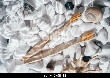 Due eco spazzolini in bambù con setole naturali in acqua dolce trasparente con flocchi e onde sul fondo di pietre bianche e conchiglie. Senza sprechi Foto Stock