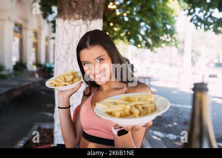 Le giovani donne tengono patatine fritte su piatti bianchi. Street cafe Foto Stock