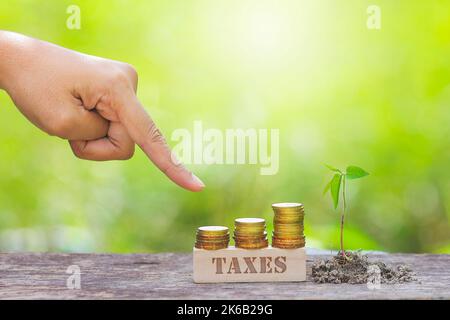 PAROLA DI TASSE CON MANO D'UOMO D'AFFARI CHE PUNTA ALLA PILA DELLA MONETA D'ORO Foto Stock