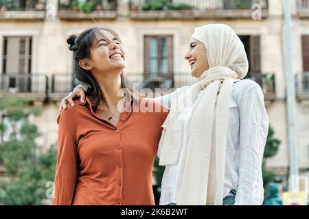 Amici femminili multietnici che si abbracciano e sorridono mentre si divertono insieme all'aperto per strada. Foto Stock