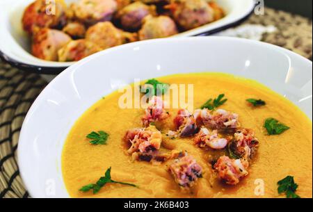 Zuppa di zucca in un recipiente di ceramica bianco con salumi e foglie di coriandolo fresco cosparse sulla parte superiore Foto Stock