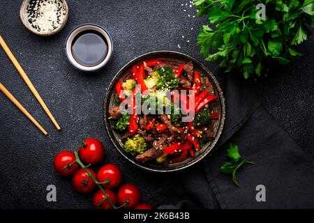 Mescolare le verdure friggete con manzo, paprika e broccoli con i semi di sesamo nel recipiente su sfondo nero da tavolo, vista dall'alto Foto Stock