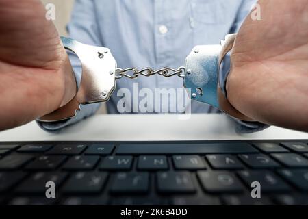 Mano uomo d'affari con manette e computer portatile. Il concetto di crimini nel cyberspazio. Foto Stock