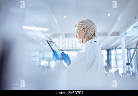 Sempre aggiornati sulle ultime tendenze. Una scienziata matura che utilizza un tablet digitale nel suo laboratorio. Foto Stock